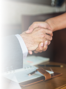 Two people shaking hands over a desk with a notebook and pen, symbolizing agreement or partnership in a professional setting.